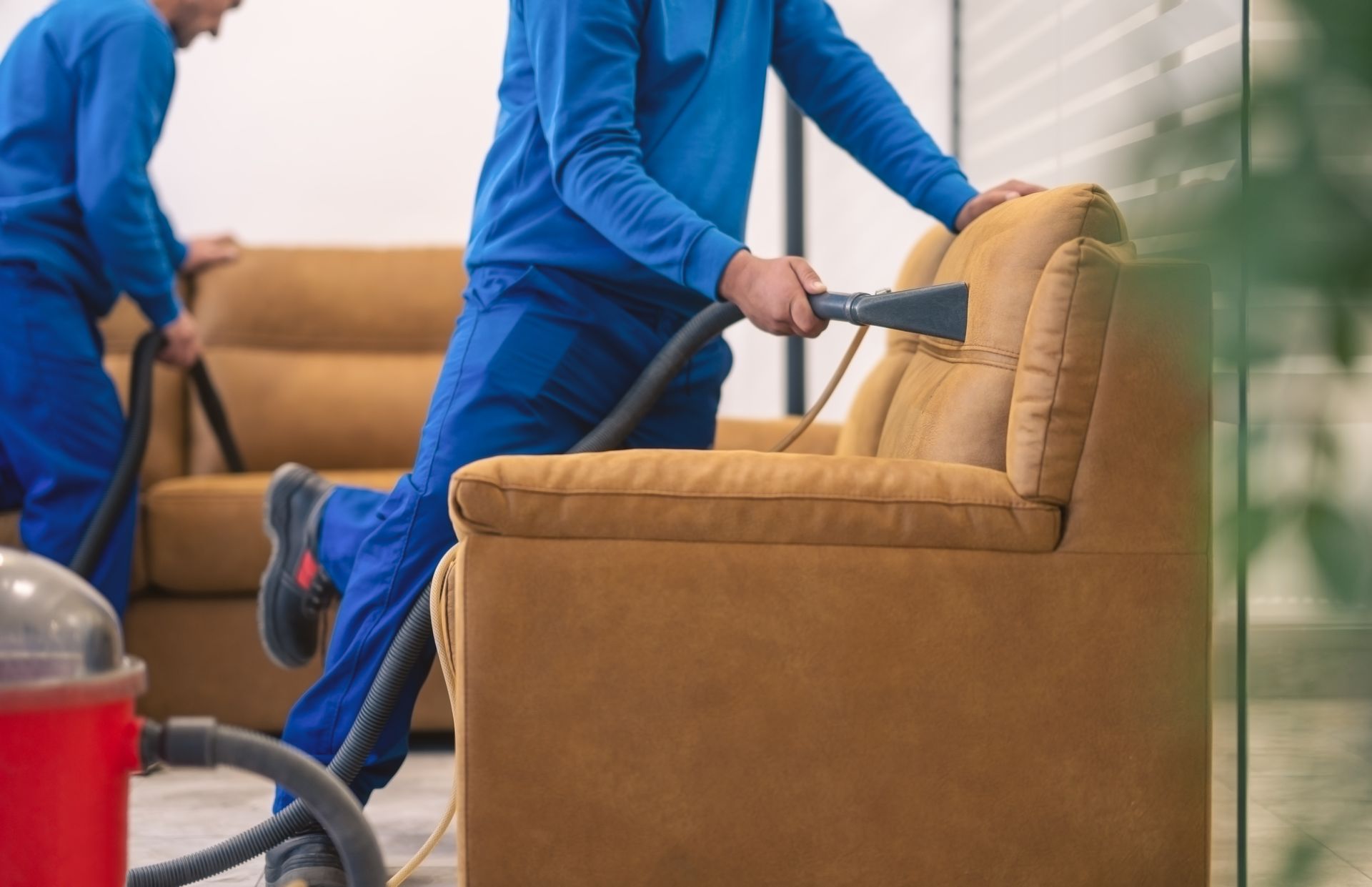 Professional cleaning technician steam cleaning tan upholstered armchair in blue uniform